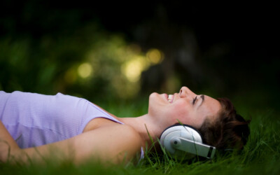 Young attractive girl listening to headphones lying on grass