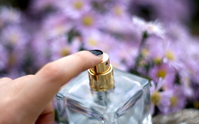 Unrecognizable person spraying perfume. Selective focus, purple flowers in the background.